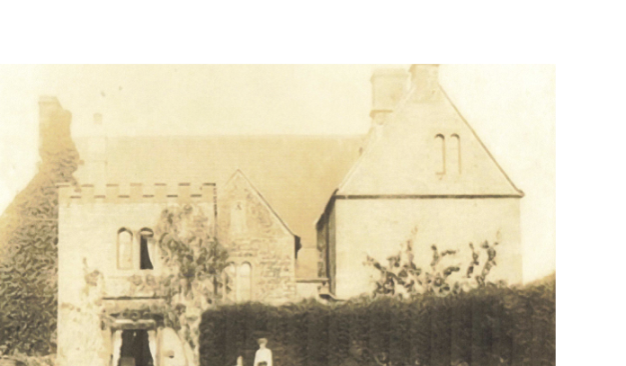 Early photograph of the west elevation of Old Manor Farm, with a figure in the foreground and the church tower visible beyond